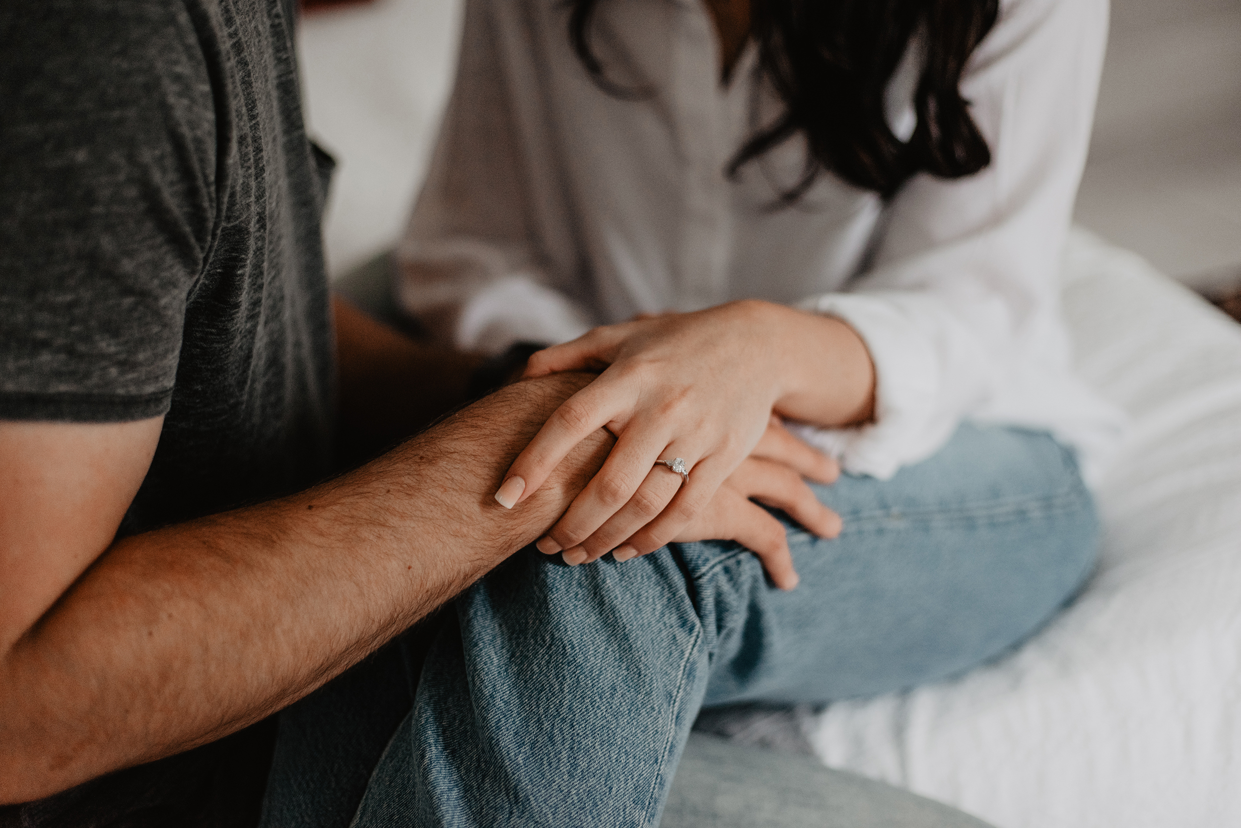 Close up of two people sitting together, with one person gently placing a hand on the other’s arm in a supportive gesture.